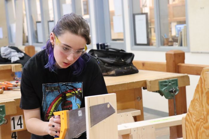 female student using a hand saw to cut a piece of wood