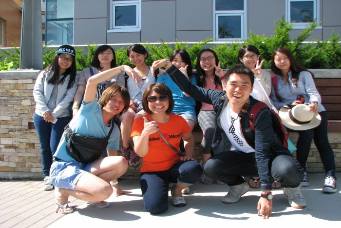 A group of young adults posing for a photo in front of a stone wall, with several people making heart shapes with their hands.