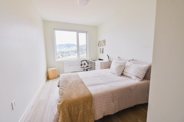 Comfortable queen-size bed positioned beside a window that brings natural light into the studio, creating a bright and inviting sleeping area.