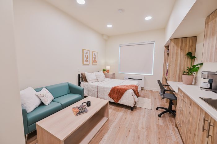 Bright, inviting studio room featuring a queen bed, a fully equipped kitchen, and a cozy seating area with a couch and coffee table, all arranged in a comfortable, modern space.