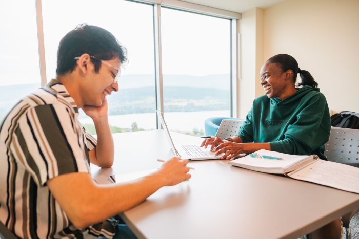wo students sitting together in the lounge, studying and smiling in a comfortable shared space.