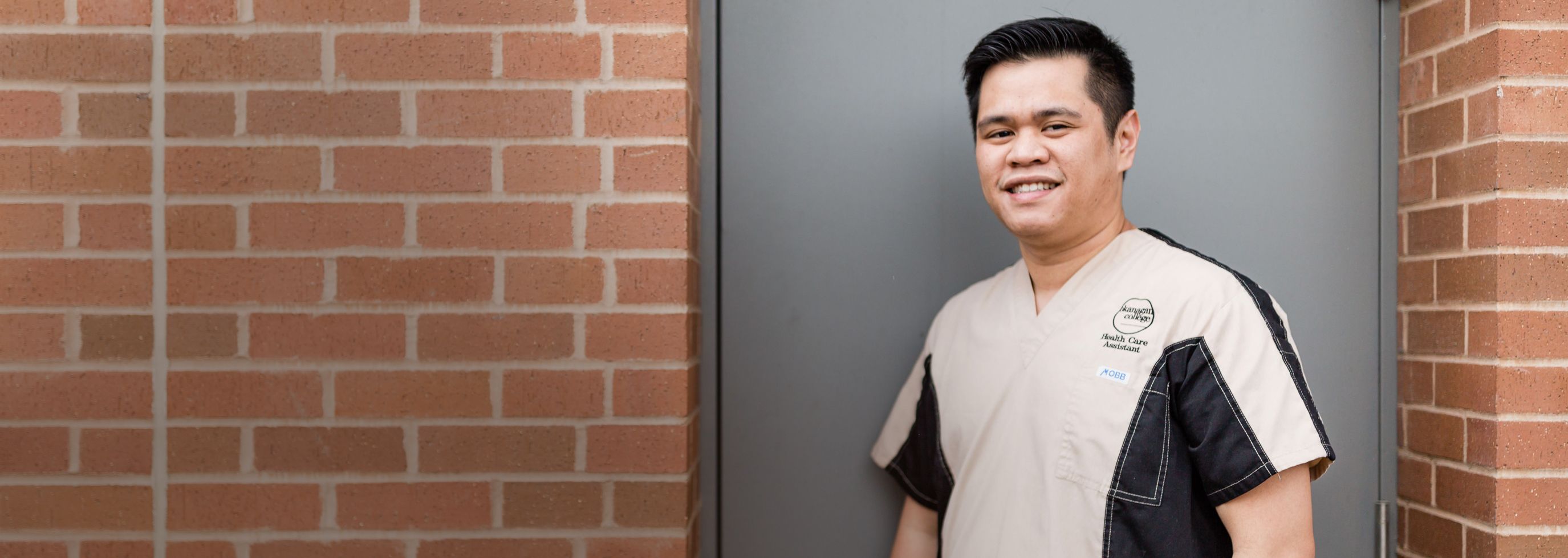 Male health student standing by a brick wall wearing his OC health program uniform shirt