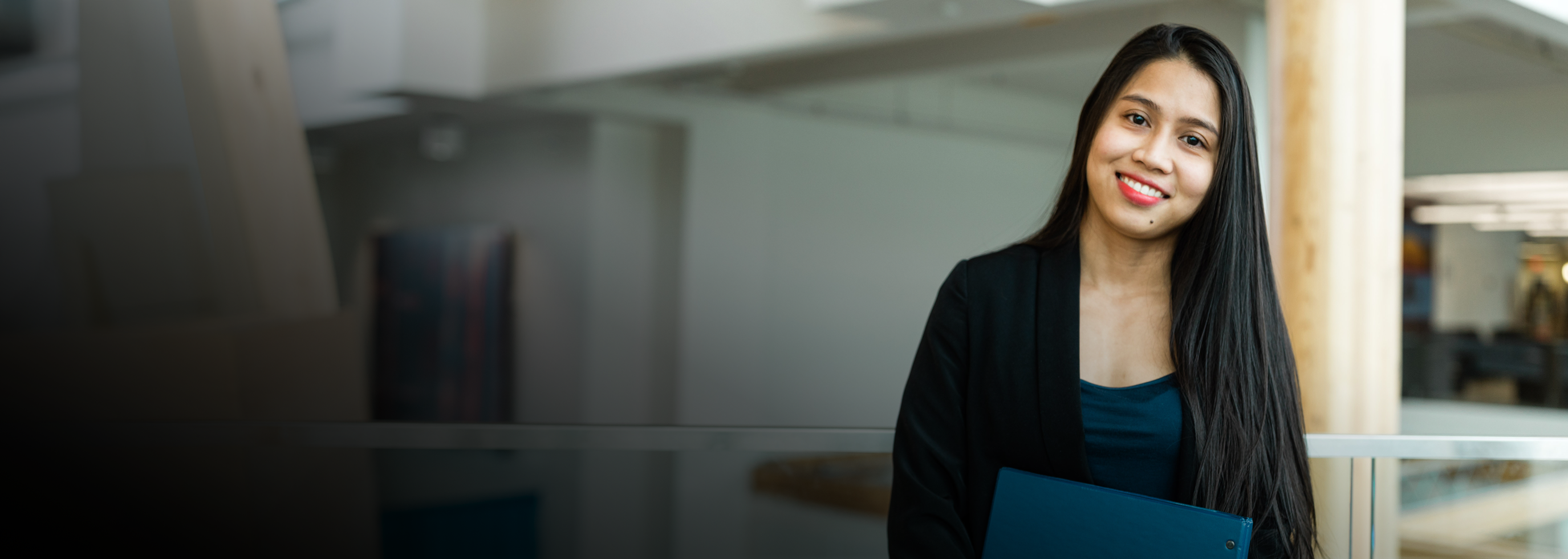 Smiling female student holding a binder in the atrium of the Centre for Learning
