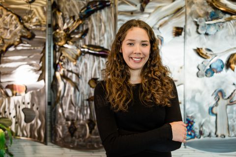 Indigenous female student standing with arms crossed in front of Indigenous art.