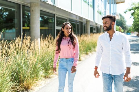 Two international students, one female and one male, walking outside on a sunny day.