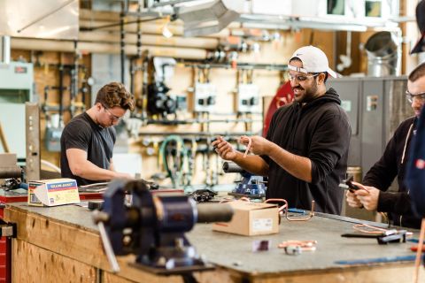 Male students wearing safety glasses work on refrigeraters and air conditioners.