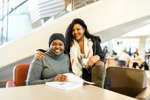 two students sitting at table and reading textbook