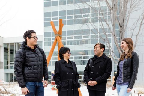 four students standing outside the snow with books and bags