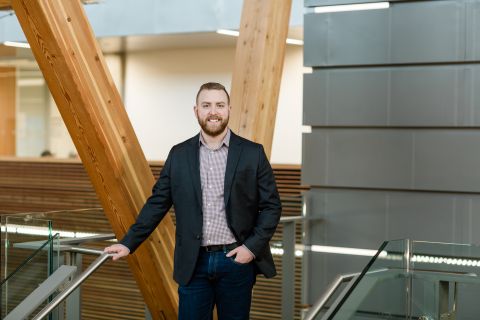 A male student wearing a blazer and dress shirt stands in the stairwell of the Trades building.