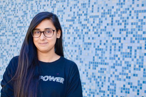 Student standing in front of a blue tile wall