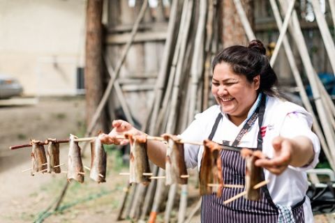 Culinary Arts student shows off salmon fillets on stakes that will go onto the fire.