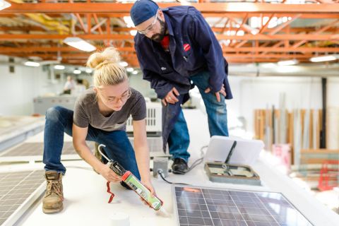 An RV Repair student applies caulking to a roof seal while an instructor looks on