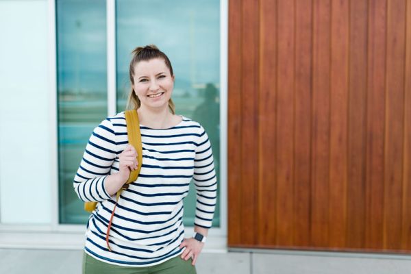 Students smiling outside with backpack on one shoulder.