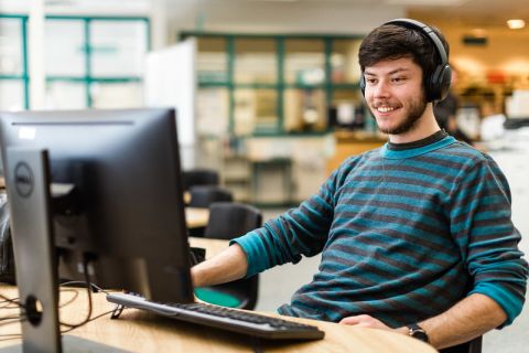 Student with headset looking at computer screen smiling