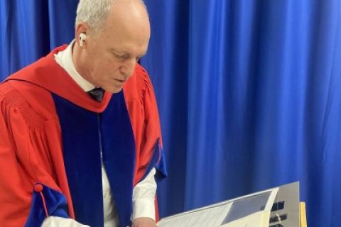 Jim Hamilton in regalia signs documents on a podium
