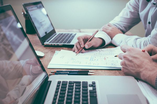 Two hands pointing at paperwork in between two laptops