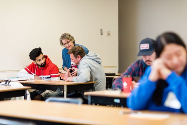 Instructor helping two students sitting a desk in a classroom