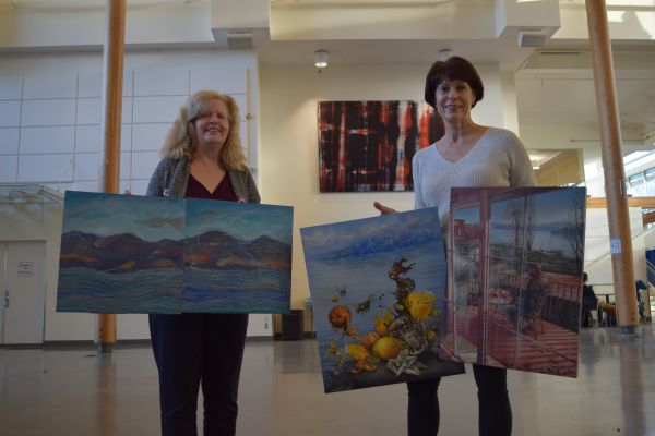 Two women show their paintings to the camera at the Centre for Learning atrium