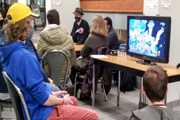 Students are playing video games while other students talk to each other in the background.