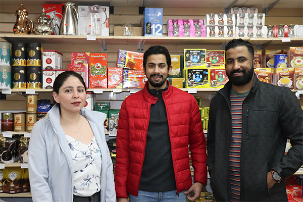 A woman and two men pose in front of their shelve full of merchandise