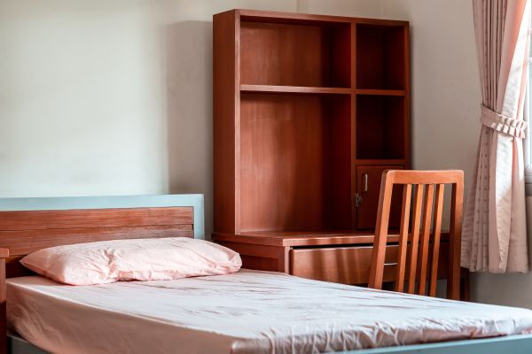 A bed and desk sit in a room with curtains by the window.