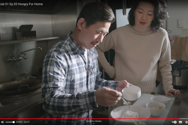 Chef Han Lin adds sauce to his rice dish as part of his demonstration to the documentary series host in the background