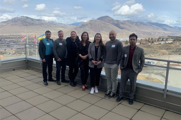 Seven OC employees stand on a TRU deck overlooking the Kamloops mountain