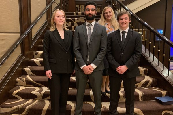 3 students wearing suits standing on a stairwell
