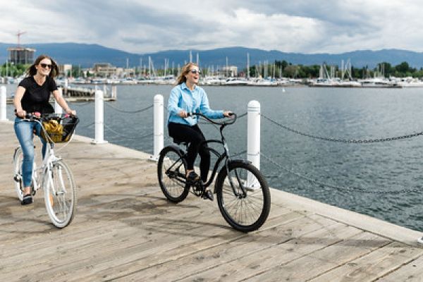 Young women riding bikes along boardwalk with Okanagan lake in background