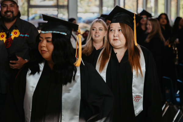 Two female students walking at convocation wearing Indigenous stoles