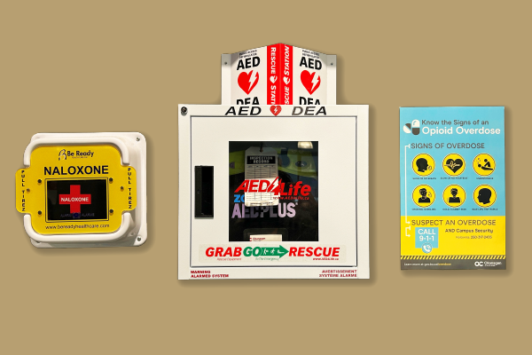 Photograph of safety station on wall at the college with Naloxone kit, AED and signs of an overdose poster