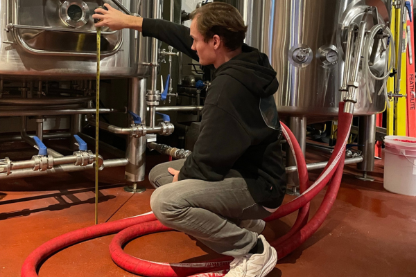 Man crouched in casual wear next to large stainless steel tanks with measuring tanks