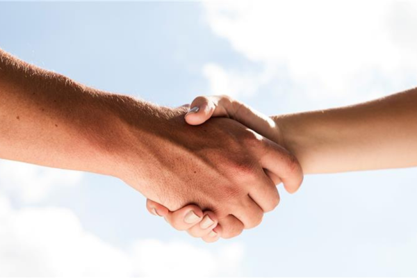 Image of two hands shaking with blue sky and clouds in background