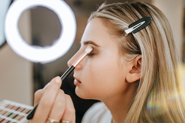 Side profile of a blonde woman having eyeshadow applied with a brush in a spa