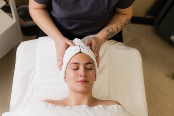 Female laying on spa table with towel wrapped around head and spa practitioners hands cradling her head