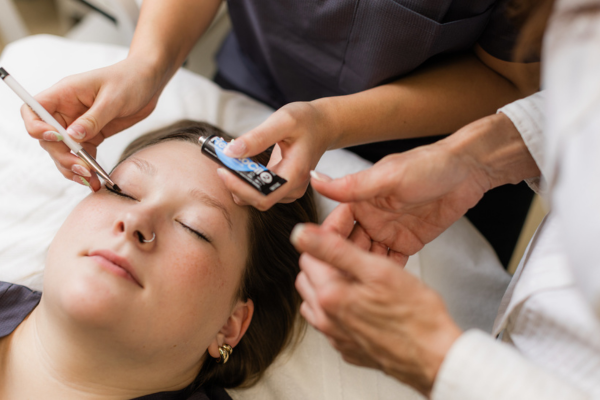 Woman lying on spa table with practitioner applying treatment to her eyelashes with a brush