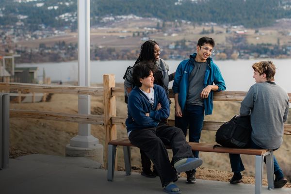 A group of OC students on a bench near a lake, taking in the tranquil scenery and enjoying their time outdoors