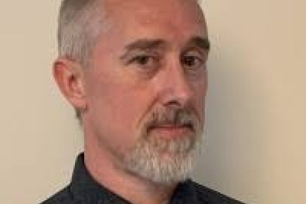 Steven Crema stands smiling infront of a while background