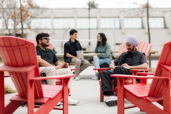 Group of students talking, seated on red chairs.