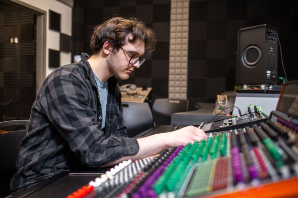 Person adjusting controls on a large audio mixing console in a professional sound studio