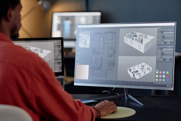 Person working on a computer with dual monitors displaying detailed 3D architectural models and layouts, representing AutoCAD
