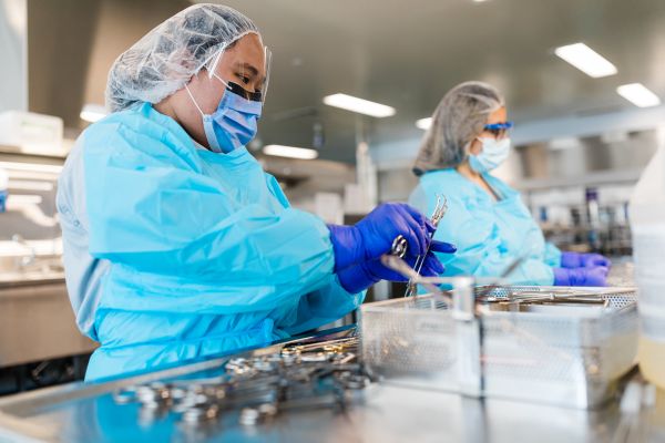 Person wearing protective gear and gloves while handling surgical instruments in a sterile processing area