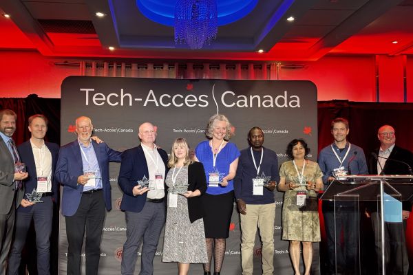 Tech-Access Canada award recipients stand together holding their trophies and smiling.