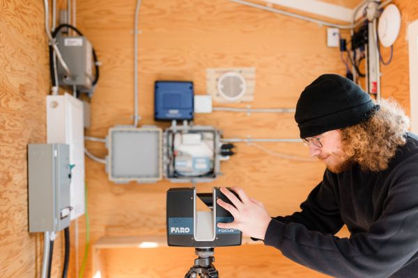 A person adjusting a FARO Focus scanner in a wooden-paneled technical room