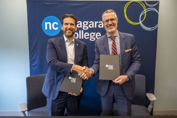 two men shaking hands and holding copies of the agreement