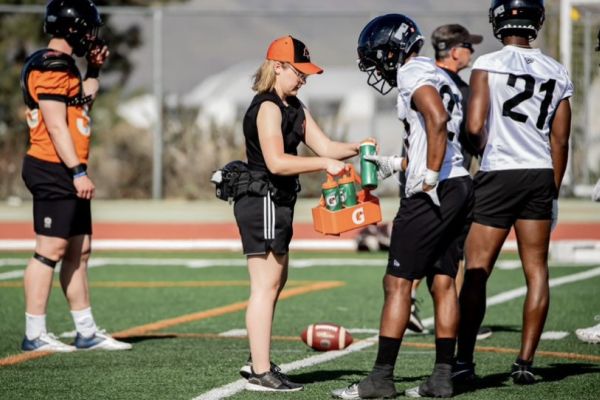 Cassidy Findlay in black shorts and orange ball cap, supports BC Lions players at training camp