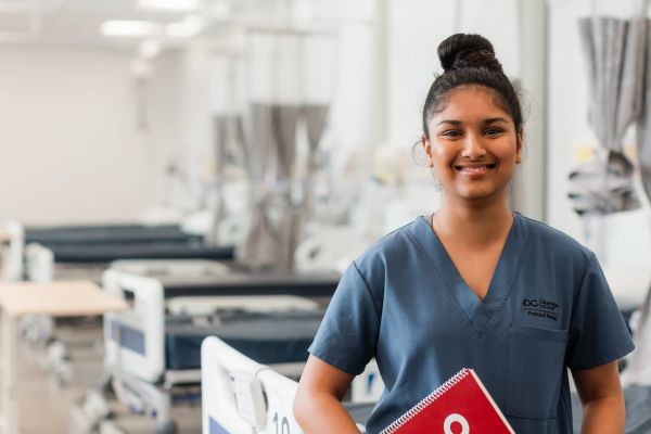 A person in scrubs in a hospital setting holding a notebook