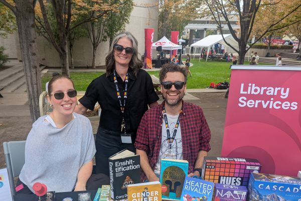Three librarians at a table during an orientation event with books and board games in the foreground