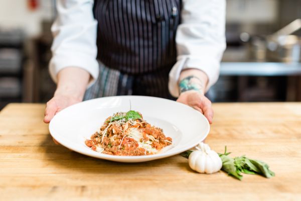 Chef presenting a plated pasta dish.