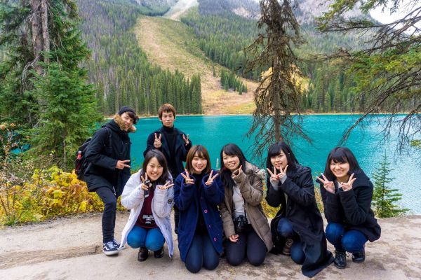 Seven young adults pose for a group photo in front of a bright blue mountain lake.